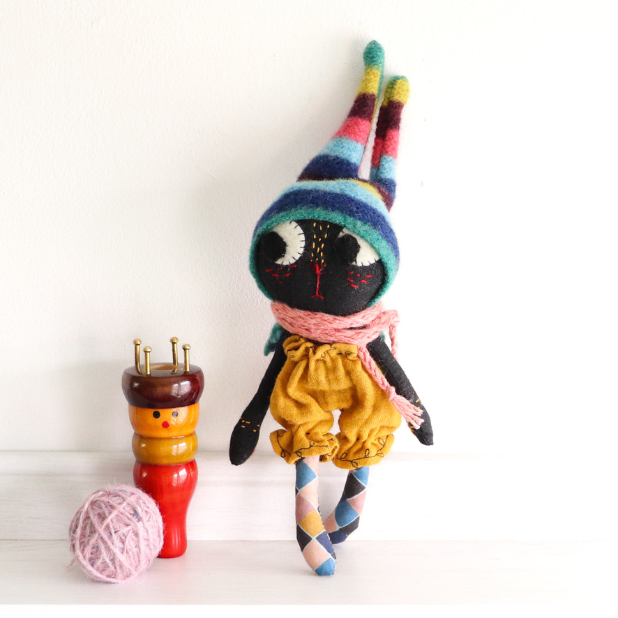 tiny kitty doll stands next to a knitting nancy