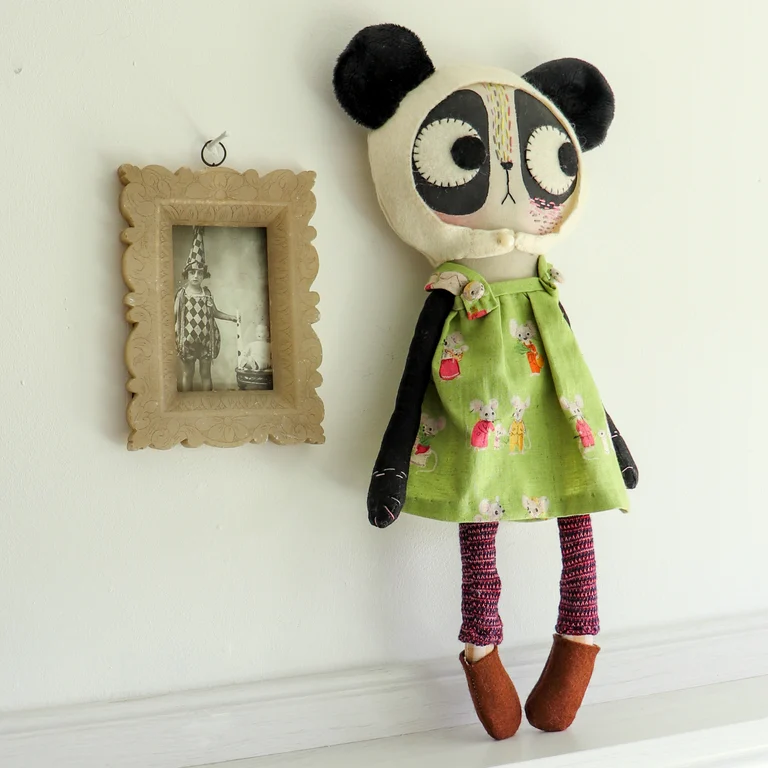 cloth panda cat doll, standing on a shelf beside a vintage photograph of a child in fancy dress, in a soapstone frame.