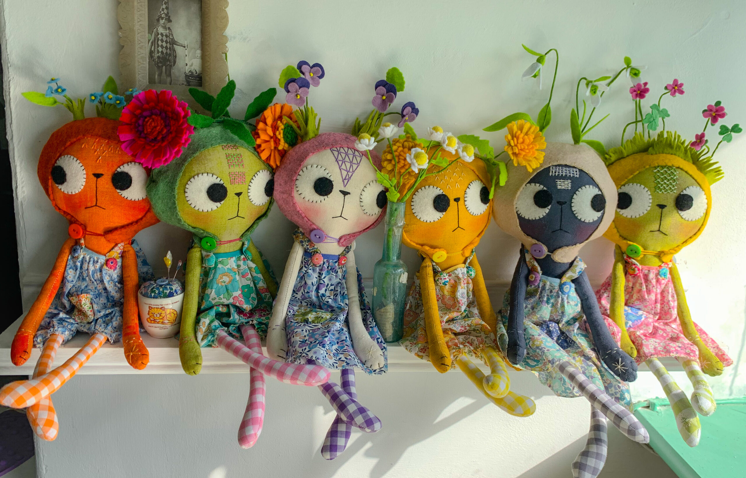 flower clad cat dolls sitting on a shelf in the sunshine