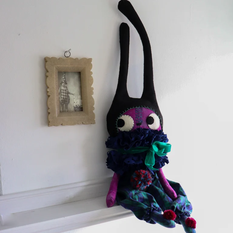purple cat doll in a tall hat, sitting on a shelf with a vinatage photograph of a child in fancy dress, in a soapstone frame