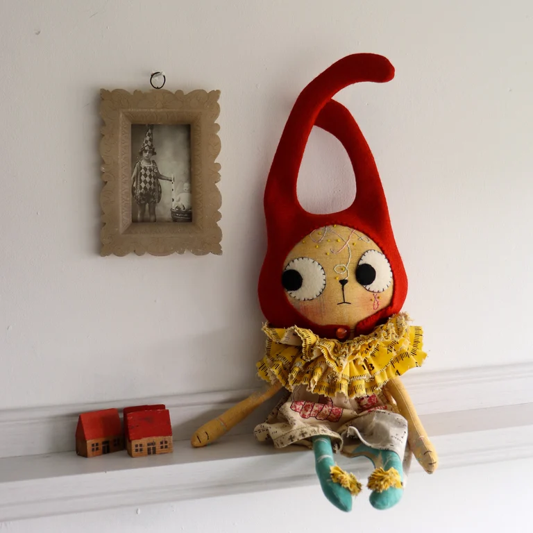 cloth cat doll sits on a shelf beside some vintage wooden toy houses.